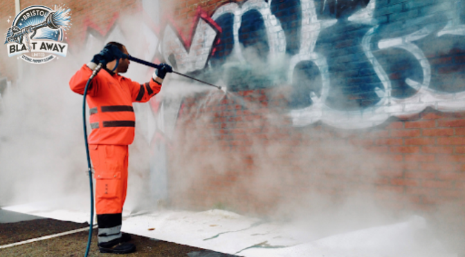 A man removing graffiti from wall by pressure washer